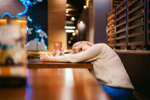 Cute young blonde woman drinks hot coffee from a glass cup in the interior of a coffee house