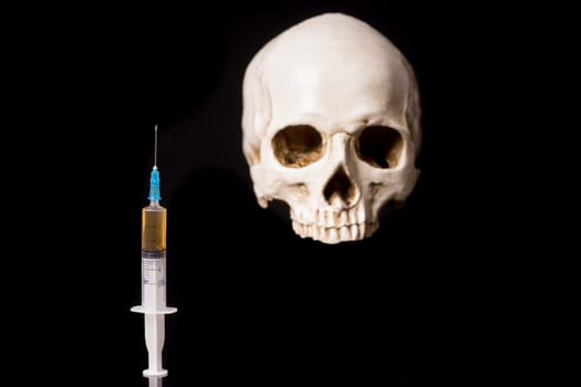 Syringe with brown liquid and blurry skull isolated on black background