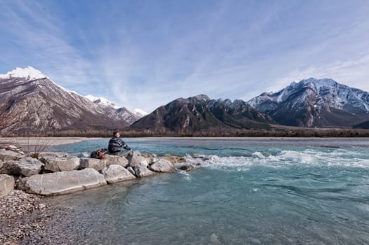Man hiker enjoys view of the river and mountains. Alps Italy Friuli Venezia Giulia.