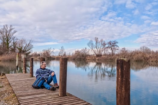 Nature landscape. Senior hiker with backpack over the wood pier on shore of river.