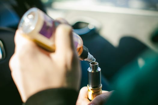 young vaper man with beard vaping mechanical mod. Guy smokes an electronic cigarette by blowing a smoke vapor. Holds in hand Refills rda juice from a bottle