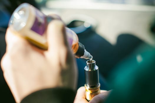 young vaper man with beard vaping mechanical mod. Guy smokes an electronic cigarette by blowing a smoke vapor. Holds in hand Refills rda juice from a bottle