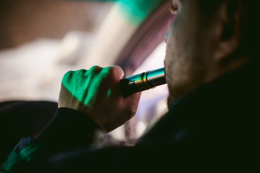 young vaper man with beard vaping mechanical mod. Guy smokes an electronic cigarette by blowing a smoke vapor. Bringing rda mouthpiece to the lips on colorful background
