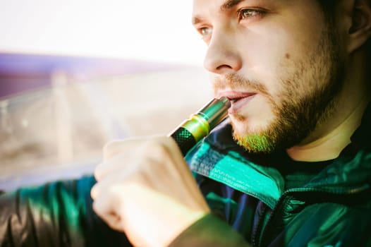 young vaper man with beard vaping mechanical mod. Guy smokes an electronic cigarette by blowing a smoke vapor. Bringing rda mouthpiece to the lips on colorful background