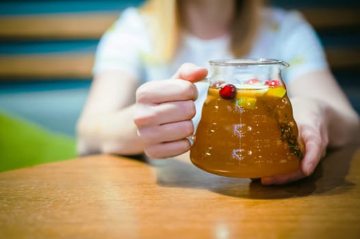 Young blonde woman wearing white T-shirt with print, girl Holds a glass jug in his hand, sitting at a table in a cafe, background stylized Wood texture lit up with warm light