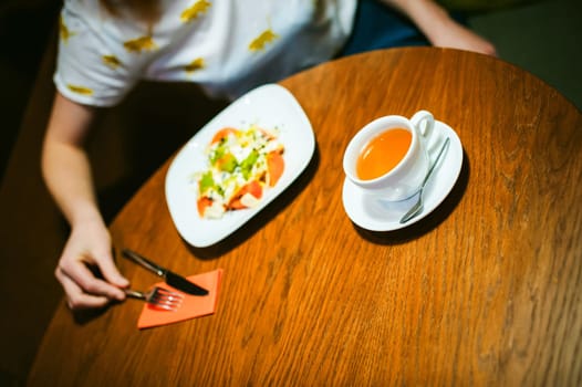 Young blonde woman wearing white T-shirt with print, girl Eats salad at lunch time, sitting at a table in a cafe, background stylized Wood texture lit up with warm light