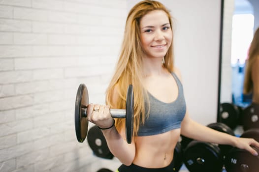 girl in a bright white gym. Two young athletic women near sports equipment are preparing for the traning with dumbbells, holding up in their hands. Healthy way of life, good spirits