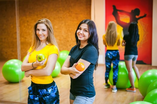 Two young athletic physique women in gym. Fitness girl with fruits, lifestyle in losing weight and diets, proper nutrition, exercise