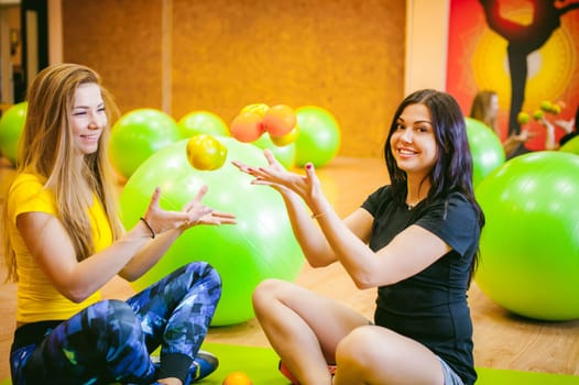 Two young athletic physique women in gym. Fitness girl with fruits, lifestyle in losing weight and diets, proper nutrition, exercise