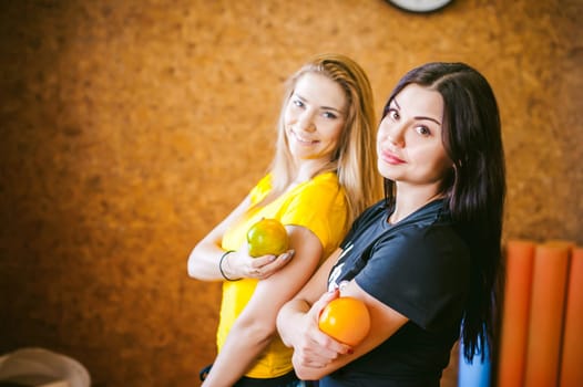 Two young athletic physique women in gym. Fitness girl with fruits, lifestyle in losing weight and diets, proper nutrition, exercise