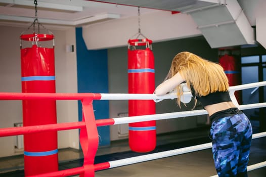young woman in boxing gloves on a ring. girl looks tired, leaned on the ropes, after training in martial arts