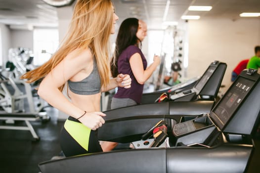 young woman is engaged fitness in gym. Performs cardio load on treadmill, running and walking with acceleration. sport, fit, lifestyle, technology and people concept