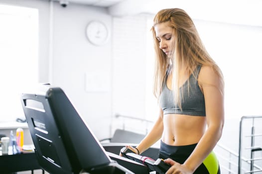 young woman is engaged fitness in gym. Performs cardio load on treadmill, running and walking with acceleration. sport, fit, lifestyle, technology and people concept