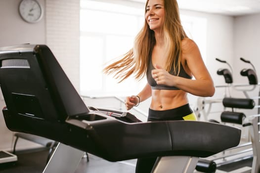 young woman is engaged fitness in gym. Performs cardio load on treadmill, running and walking with acceleration. sport, fit, lifestyle, technology and people concept