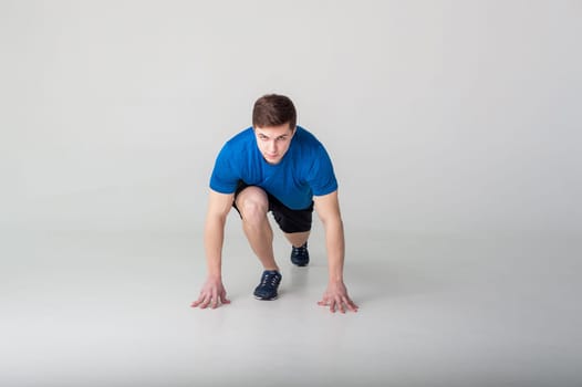 Running man on low start. Stands in rack, ready to achieve goals and wins. Young sexy Muscular male athlete wearing sporty blue t-shirt and shorts, studio portrait white background.Motivation concept