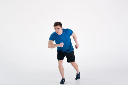 Running man on low start. Stands in rack, ready to achieve goals and wins. Young sexy Muscular male athlete wearing sporty blue t-shirt and shorts, studio portrait white background.Motivation concept