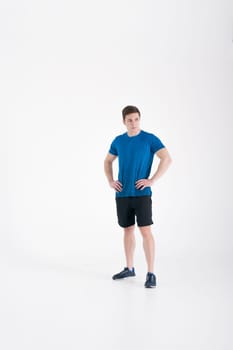 Young muscular handsome athletic man dressed in blue sport shirt, shorts and sneakers standing on white background in studio, Holding hands at waist