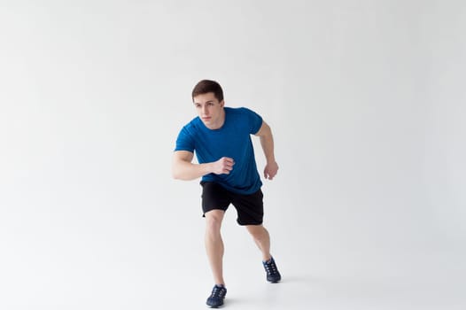 Running man on low start. Stands in rack, ready to achieve goals and wins. Young sexy Muscular male athlete wearing sporty blue t-shirt and shorts, studio portrait white background.Motivation concept