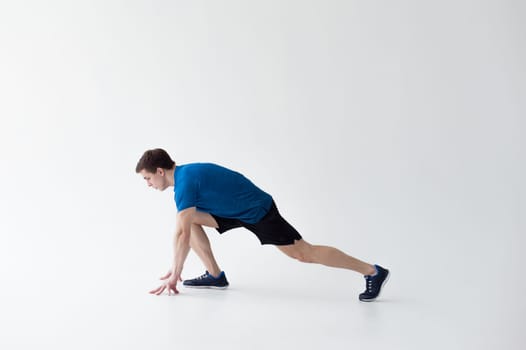Running man on low start. Stands in rack, ready to achieve goals and wins. Young sexy Muscular male athlete wearing sporty blue t-shirt and shorts, studio portrait white background.Motivation concept