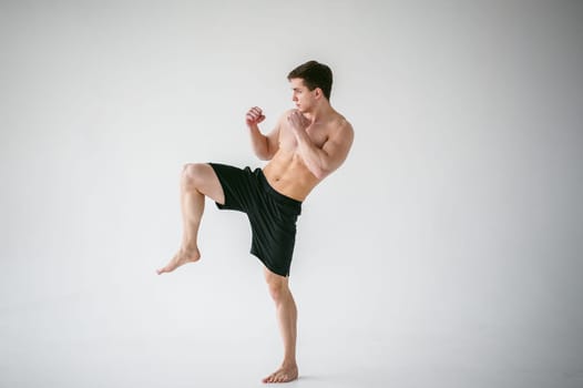 young sexy handsome men strong Athlete's body with bare torso, Dressed black sports shorts, portrait of studio of light-skinned strong man standing in fighting stance Kicking, straining powerful legs