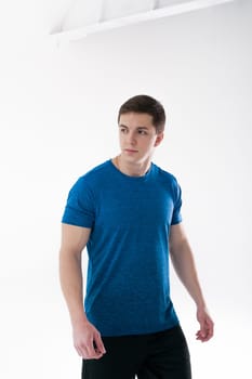 Young muscular handsome athletic man dressed in blue sport shirt, shorts and sneakers standing on white background in studio