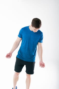 Young muscular handsome athletic man dressed in blue sport shirt, shorts and sneakers standing on white background in studio
