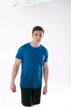 Young muscular handsome athletic man dressed in blue sport shirt, shorts and sneakers standing on white background in studio