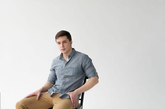 Man dressed in a shirt and brown trousers sits on a wooden vintage chair on a white background