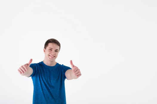 Young muscular handsome athletic man dressed in blue sport shirt standing on white background in studio, Shows thumbs up and smiles