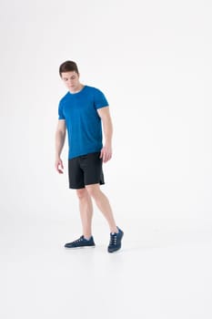 Young muscular handsome athletic man dressed in blue sport shirt, shorts and sneakers standing on white background in studio, Taking a step