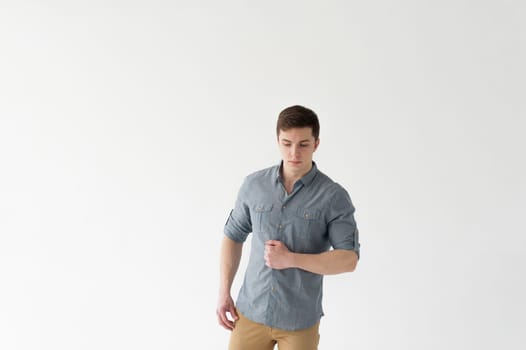 Young handsome man of strong athletic build, dressed in a shirt and brown trousers, Posing on white studio background