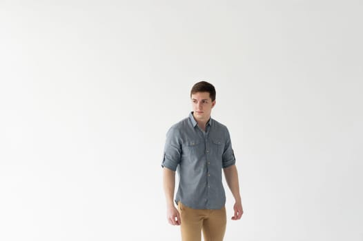 Young handsome man of strong athletic build, dressed in a shirt and brown trousers, Posing on white studio background