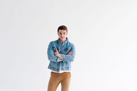Young handsome man of strong Athlete's body, dressed in Blue jeans jacket in style of old school and white t-shirt with brown trousers, Posing on white studio background, With his arms crossed