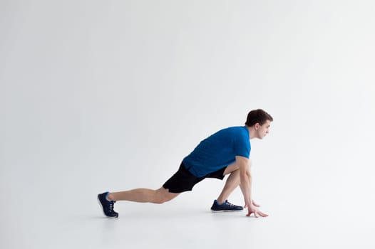 Running man on low start. Stands in rack, ready to achieve goals and wins. Young sexy Muscular male athlete wearing sporty blue t-shirt and shorts, studio portrait white background.Motivation concept