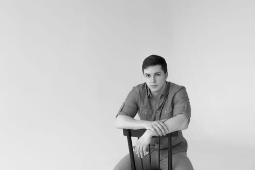 Man dressed in a shirt and brown trousers sits on a wooden vintage chair on a white background