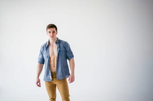 portrait young sexy handsome man of strong Athlete's body with bare torso, Dressed in an unbuttoned shirt and brown trousers, Posing on white studio background