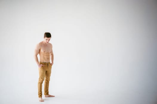 portrait young sexy handsome man of strong Athlete's body with bare torso, Dressed  brown trousers, Posing on white studio background