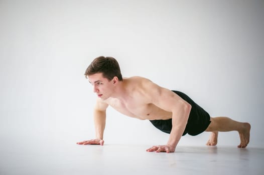 young sexy handsome men of strong Athlete's body with bare torso, Dressed black sports shorts, portrait of studio of light-skinned strong man engaged in push-ups, on floor, straining powerful hands