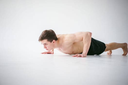 young sexy handsome men of strong Athlete's body with bare torso, Dressed black sports shorts, portrait of studio of light-skinned strong man engaged in push-ups, on floor, straining powerful hands