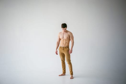 portrait young sexy handsome man of strong Athlete's body with bare torso, Dressed  brown trousers, Posing on white studio background