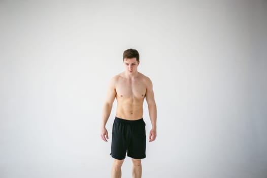 portrait young sexy handsome man of strong Athlete's body with bare torso, Dressed in a black sports shorts, Posing on white studio background