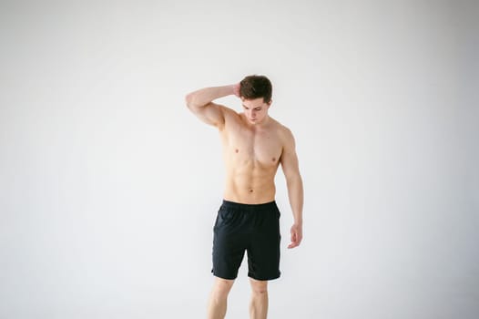 portrait young sexy handsome man of strong Athlete's body with bare torso, Dressed in a black sports shorts, Posing on white studio background
