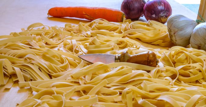 Pasta fettuccine or tagliatelle, a tipical italian eggs pasta, ready to cook, with some vegetables in background