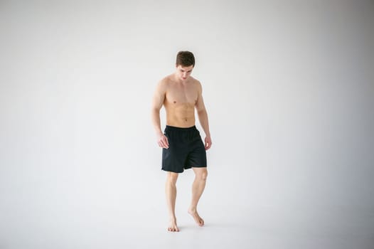 portrait young sexy handsome man of strong Athlete's body with bare torso, Dressed in a black sports shorts, Posing on white studio background