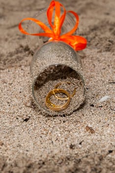 Two wedding ring inside a glass with a orange ribbon on the sand