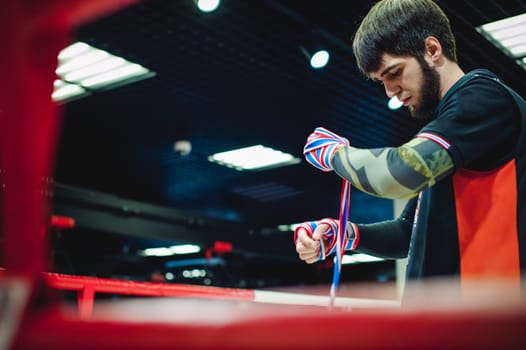 Professional Muay Thai and K1 fighter. Male boxer in training sportswear, an exercise in the sports hall, Preparation Boxing bandage