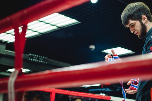 Professional Muay Thai and K1 fighter. Male boxer in training sportswear, an exercise in the sports hall, Preparation Boxing bandage