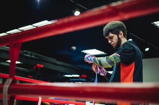Professional Muay Thai and K1 fighter. Male boxer in training sportswear, an exercise in the sports hall, Preparation Boxing bandage