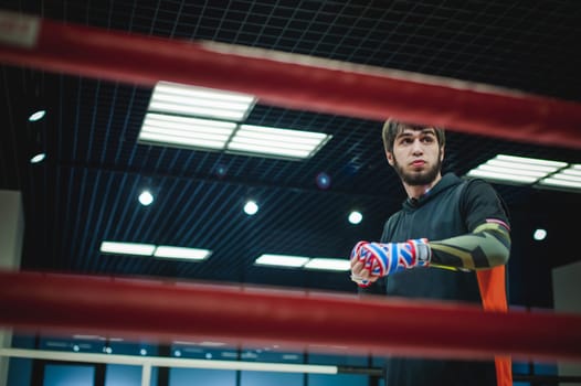 Professional Muay Thai and K1 fighter. Male boxer in training sportswear, an exercise in the sports hall, Preparation Boxing bandage
