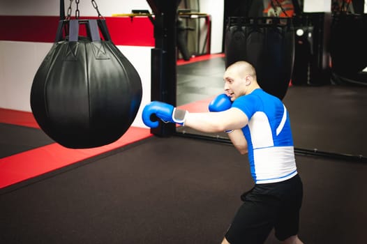 Professional Muay Thai fighter. Male boxer in training sportswear, an exercise in sports hall, Training with a punching bag, working out blows